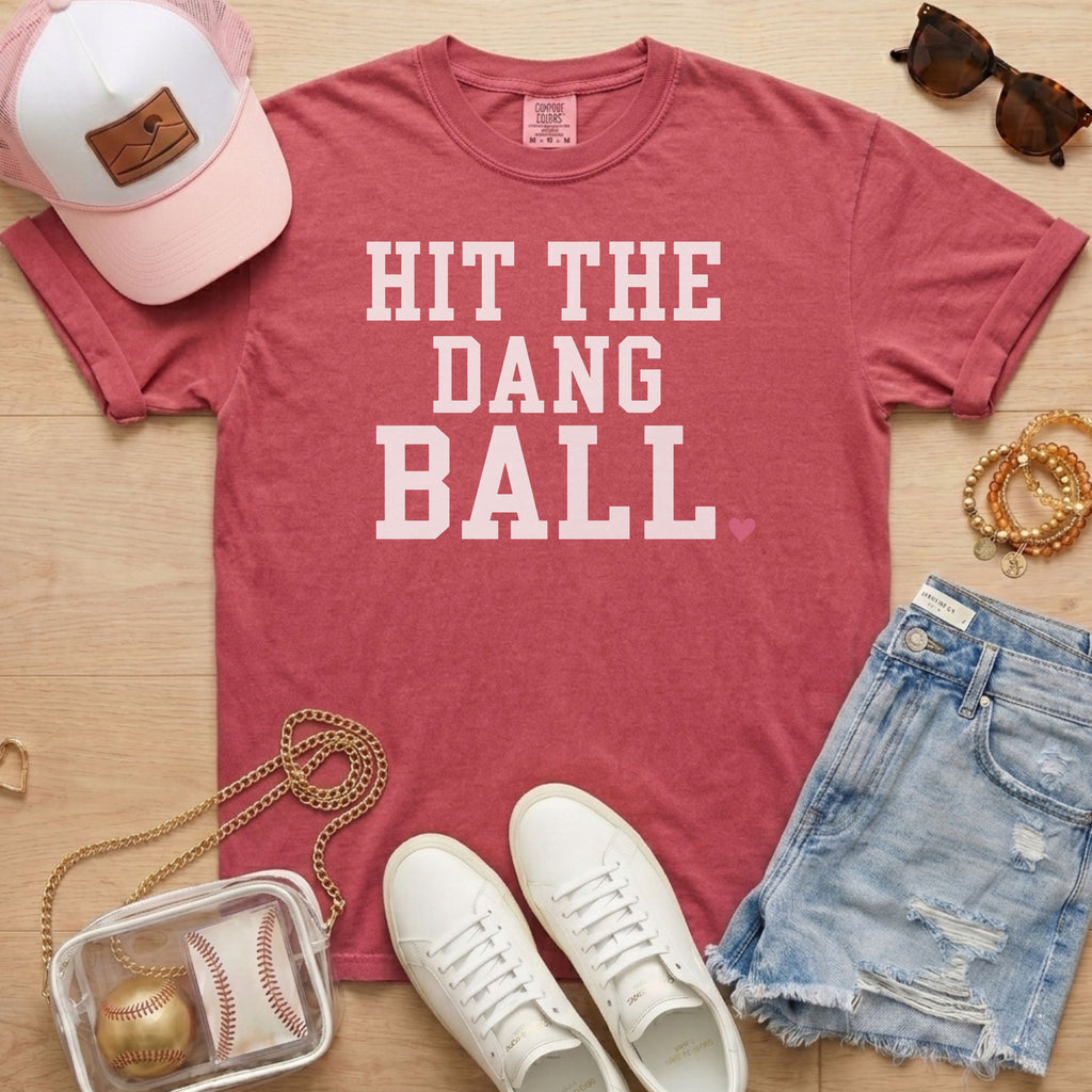 Crimson Comfort Colors sports mom shirt with Hit The Dang Ball design, styled flat lay with baseball mom game day accessories.