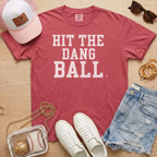 Crimson Comfort Colors sports mom shirt with Hit The Dang Ball design, styled flat lay with baseball mom game day accessories.