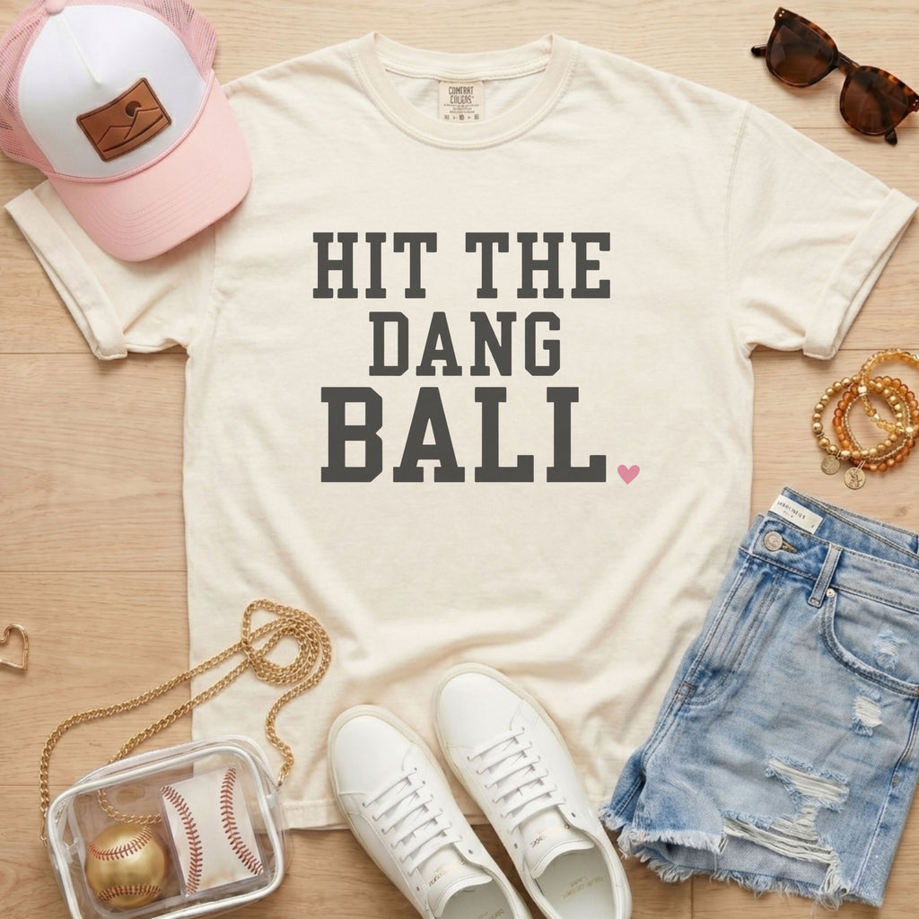 Ivory Comfort Colors baseball shirt featuring Hit The Dang Ball varsity design with pink heart, styled for a cute baseball mom outfit.