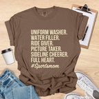 Brown t-shirt with '#Sportsmom' text on a wooden surface with accessories.