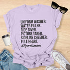 Purple t-shirt with '#Sportsmom' text on a wooden surface with sunglasses, jeans, and sneakers.