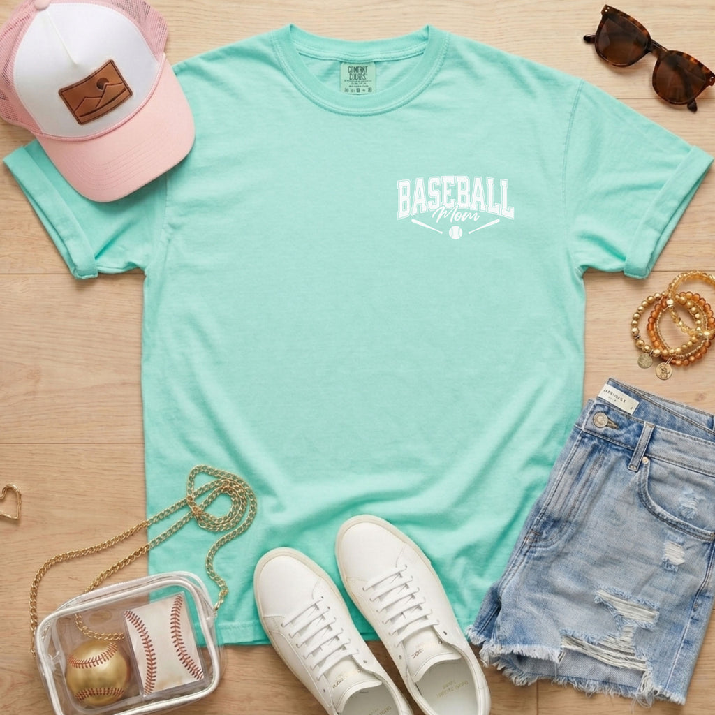 Mint green t-shirt with 'Mama Jackson' print, pink cap, white sneakers, denim shorts, and accessories on a wooden surface.