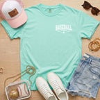 Mint green t-shirt with 'Mama Jackson' print, pink cap, white sneakers, denim shorts, and accessories on a wooden surface.