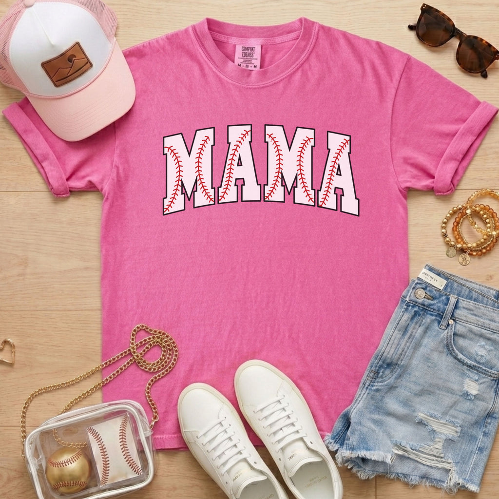 Pink t-shirt with 'MAMA' print, white sneakers, denim shorts, baseball-themed accessories on a wooden surface.