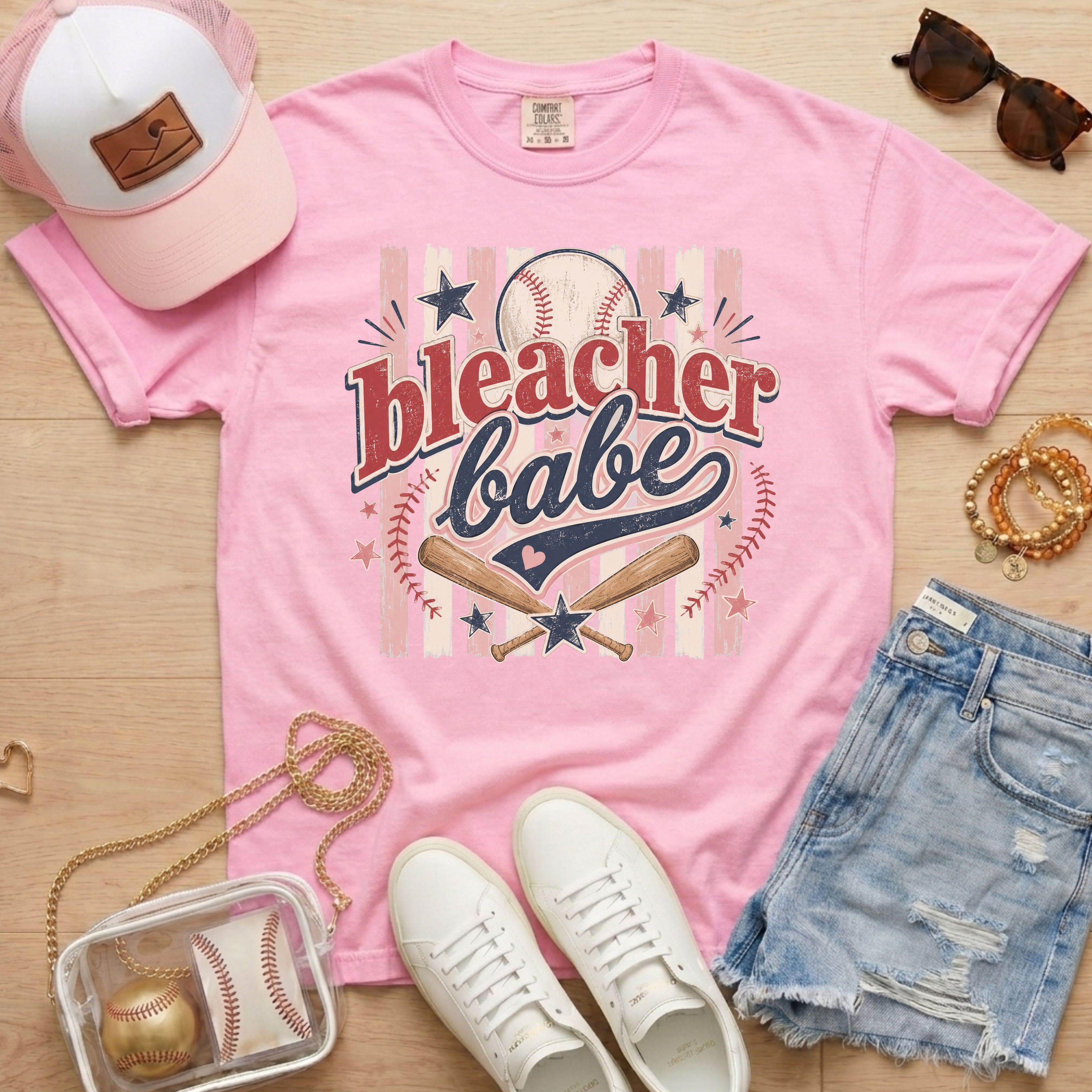 Bleacher Babe baseball mom Comfort Colors tee in blossom light pink flat lay with trucker hat, denim shorts, white sneakers, and baseball.