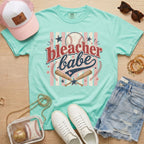 Bleacher Babe baseball mom Comfort Colors tee in chalky mint flat lay with trucker hat, denim shorts, white sneakers, and baseball.