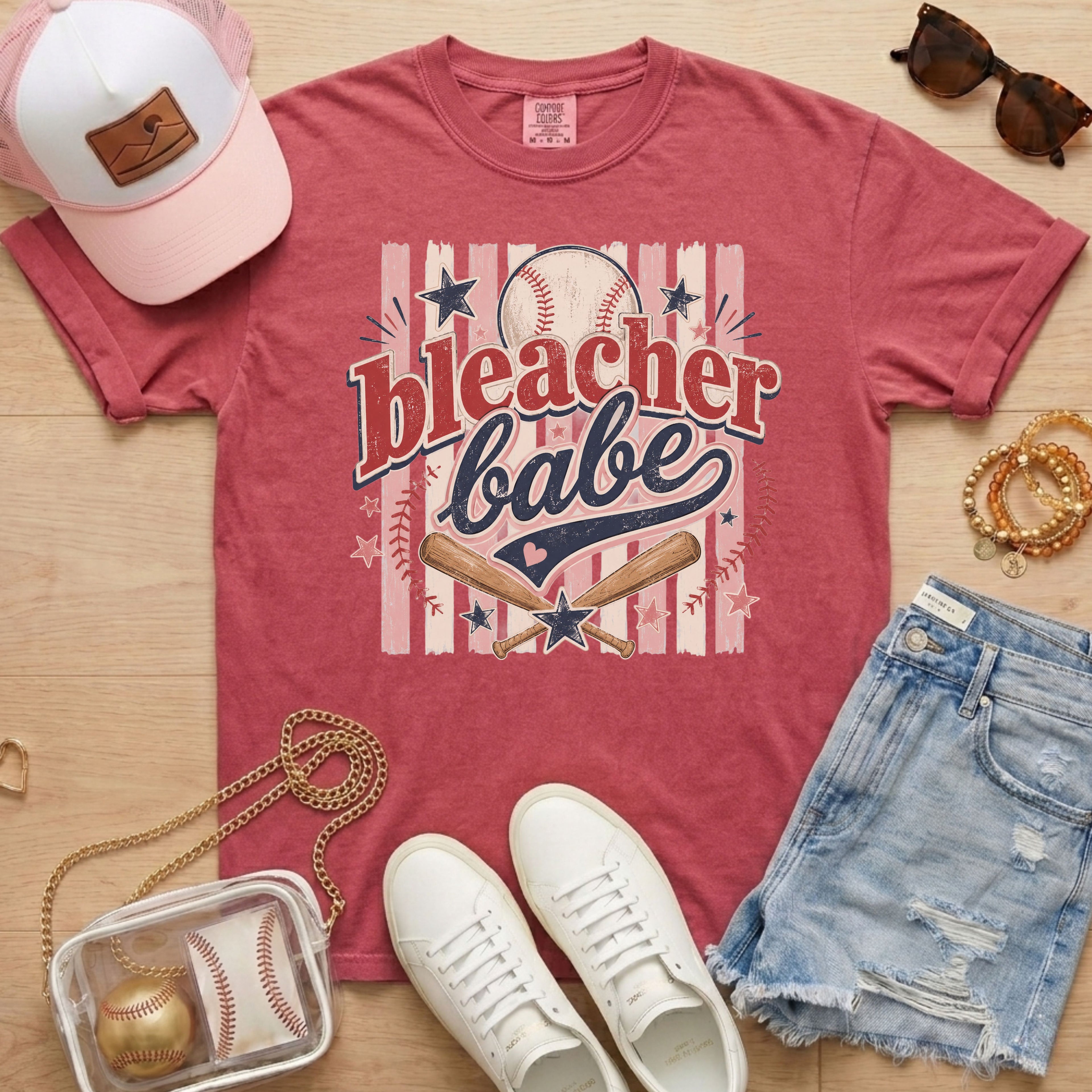 Bleacher Babe baseball mom Comfort Colors tee in crimson flat lay with trucker hat, denim shorts, white sneakers, and baseball.