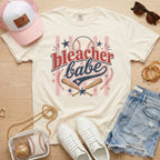 Bleacher Babe baseball mom Comfort Colors tee in ivory flat lay with trucker hat, denim shorts, white sneakers, and baseball.