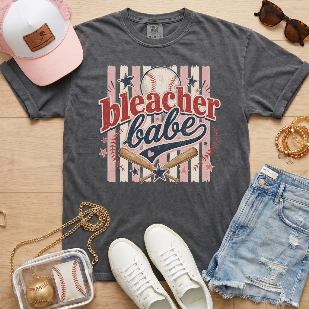Bleacher Babe baseball mom Comfort Colors tee in pepper charcoal flat lay with trucker hat, denim shorts, white sneakers, and baseball.