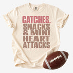 Wide receiver mom graphic T-shirt in cream, Comfort Colors Ivory, shown with a football and the “Catches, Snacks & Mini Heart Attacks” design.