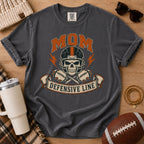 Defensive line football mom graphic T-shirt in charcoal gray, Comfort Colors Pepper, styled in a game day flat lay with a skull helmet design.
