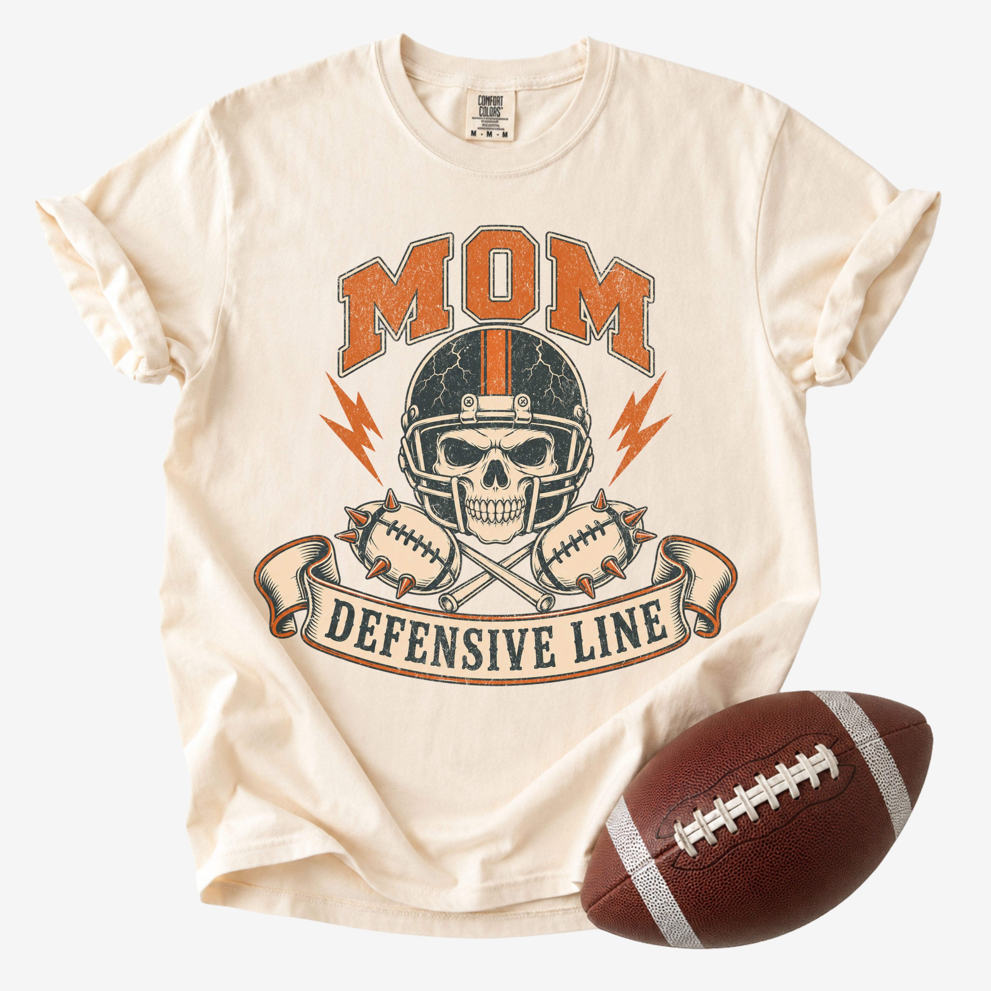Retro football mom graphic T-shirt in cream, Comfort Colors Ivory, shown from the front with a skull helmet and “Mom Defensive Line” design.