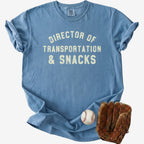 Flat lay of a distressed dusty blue t-shirt with the slogan 'DIRECTOR OF TRANSPORTATION & SNACKS' and denim shorts.