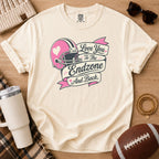 Retro football mom graphic T-shirt in cream, Comfort Colors Ivory, styled in a game day flat lay with a pink helmet and “Love You to the Endzone and Back” design.