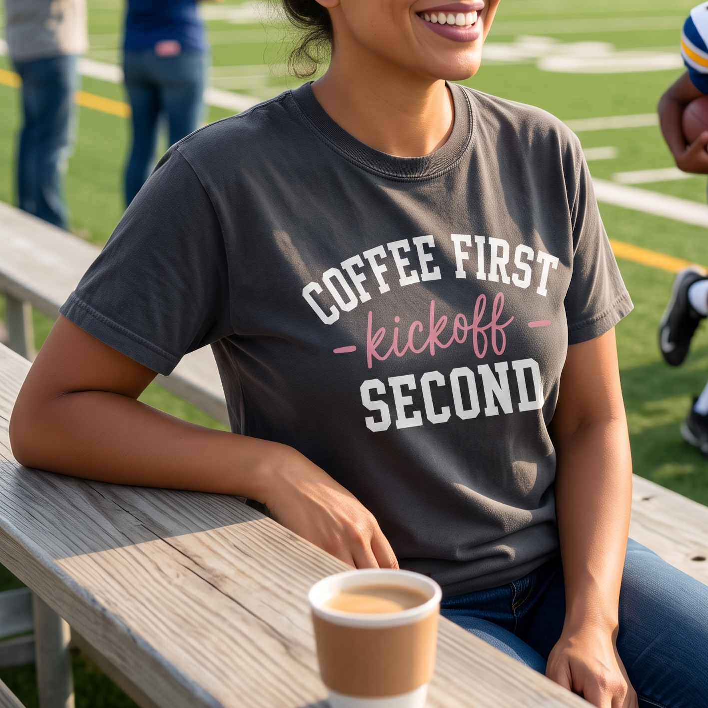 Football mom wearing a Coffee First Kickoff Second shirt while sitting near the field with coffee.
