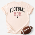 FOOTBALL MOM graphic shirt in cream, Comfort Colors Ivory, shown from the back with a football on a clean background.