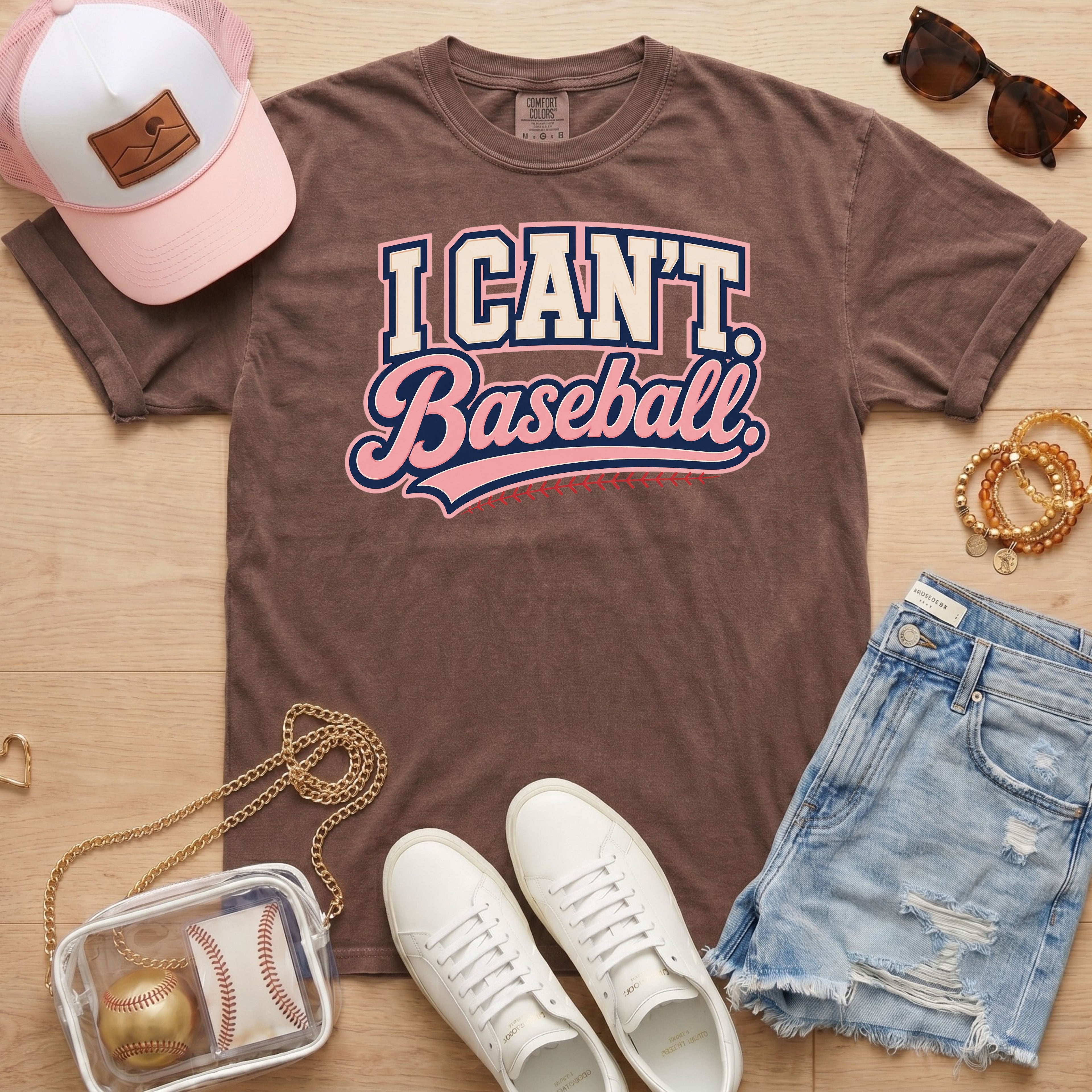 I CAN'T. Baseball. baseball mom Comfort Colors espresso tee in a boutique game day flat lay with hat, sneakers, denim shorts, and baseball bag.