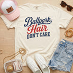 Ivory Ballpark Hair Don’t Care funny baseball mom shirt styled with denim shorts, sneakers, pink hat, clear baseball bag, and sideline accessories.