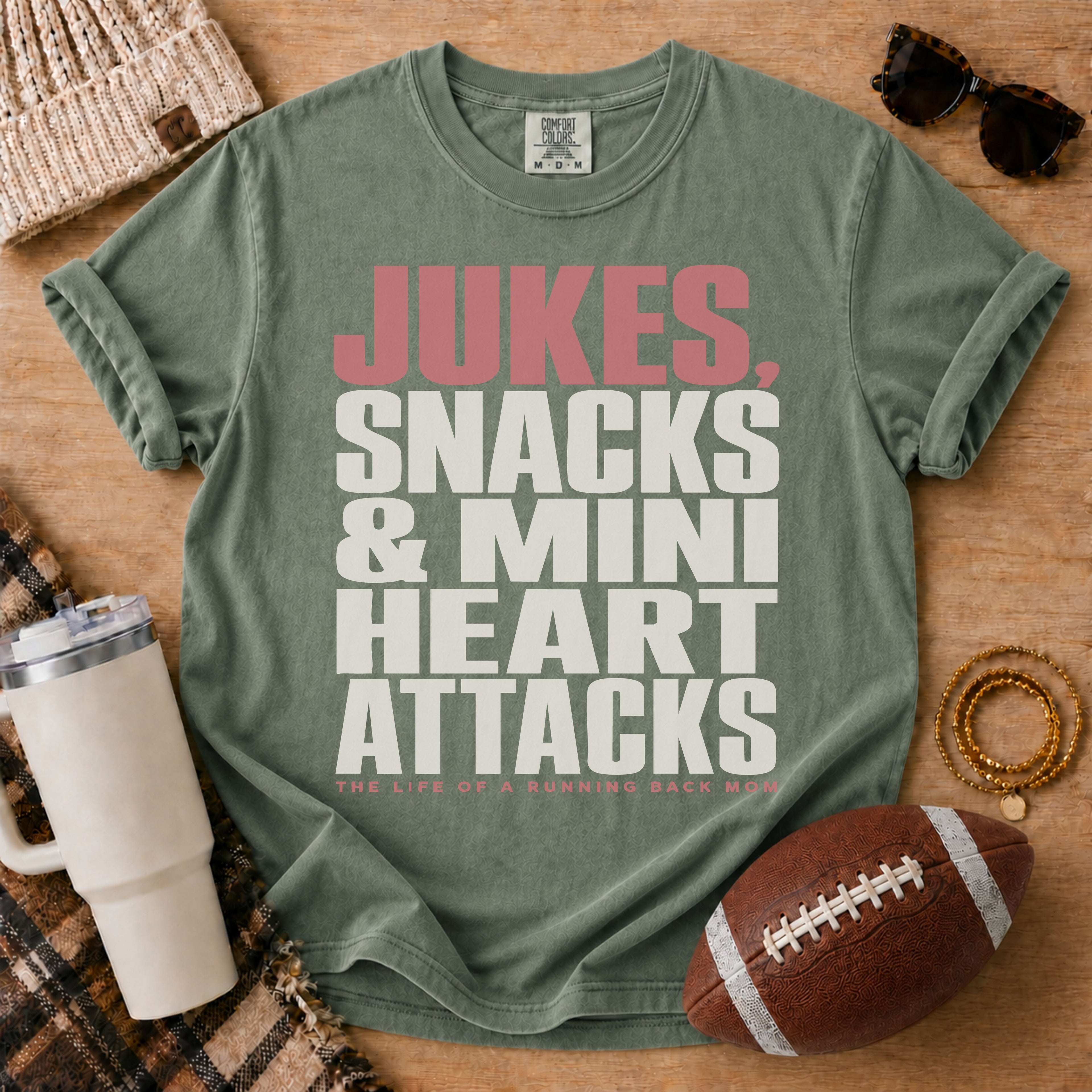 Running back football mom graphic T-shirt in olive green, Comfort Colors Moss, styled in a game day flat lay with the running back mom slogan.