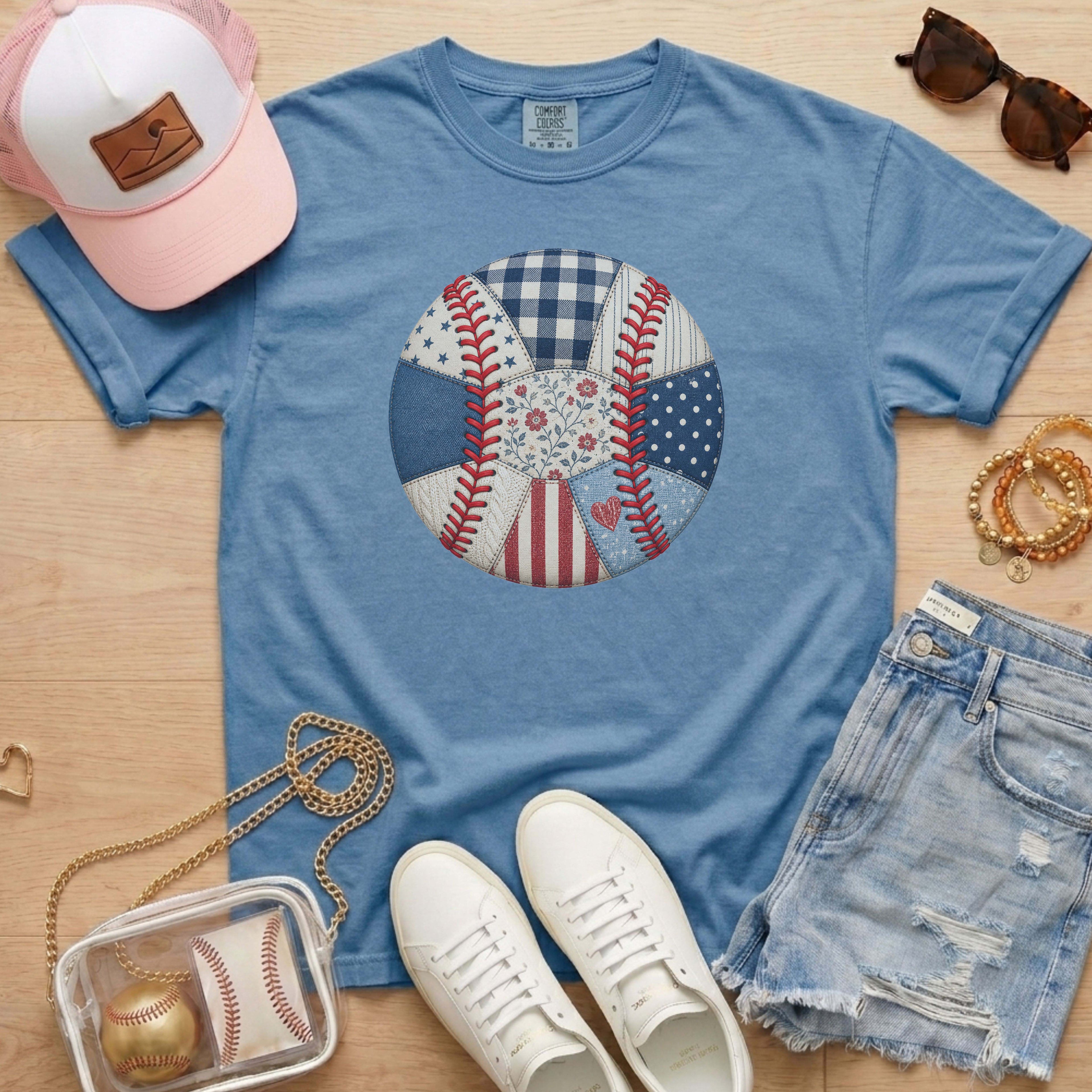 Blue t-shirt with a baseball design, white sneakers, pink cap, sunglasses, and denim shorts on a wooden surface.