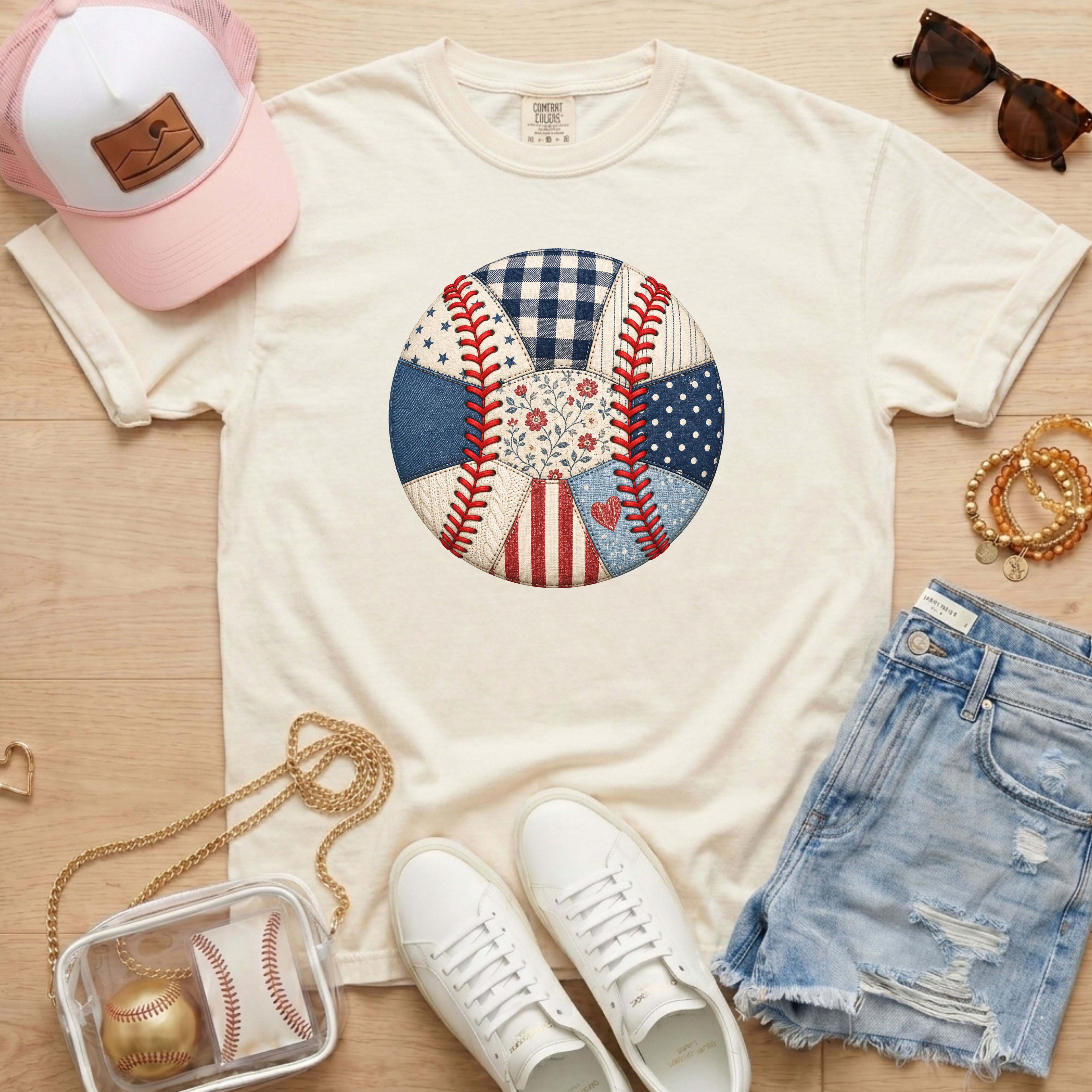 White t-shirt with a colorful patch design, white sneakers, denim shorts, pink cap, and sunglasses on a wooden surface.