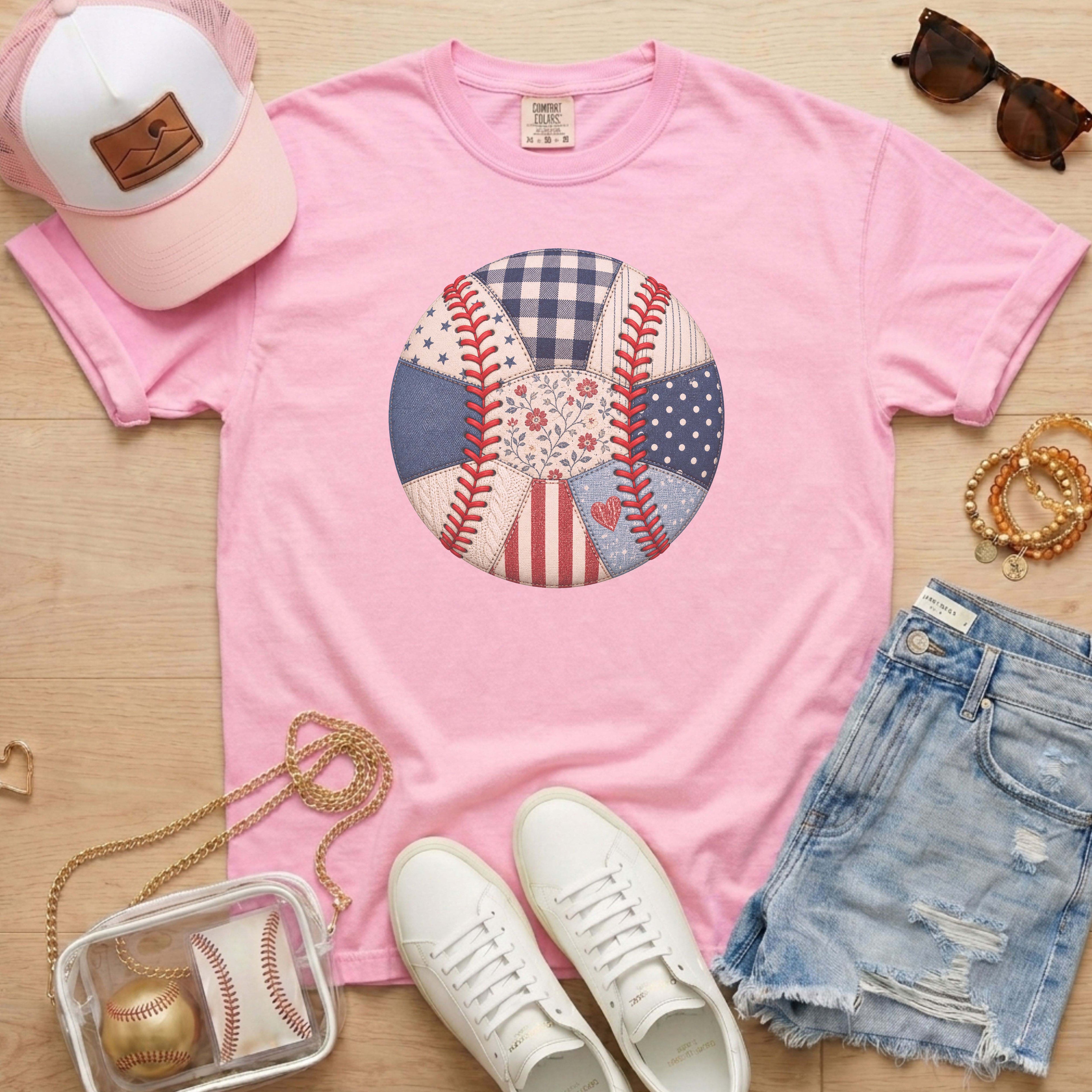 Pink t-shirt with a baseball-themed graphic, white sneakers, denim shorts, pink cap, and small handbag on a wooden surface.