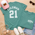Teal t-shirt with 'Coleman 21' design, pink cap, sunglasses, and baseballs on a wooden surface.