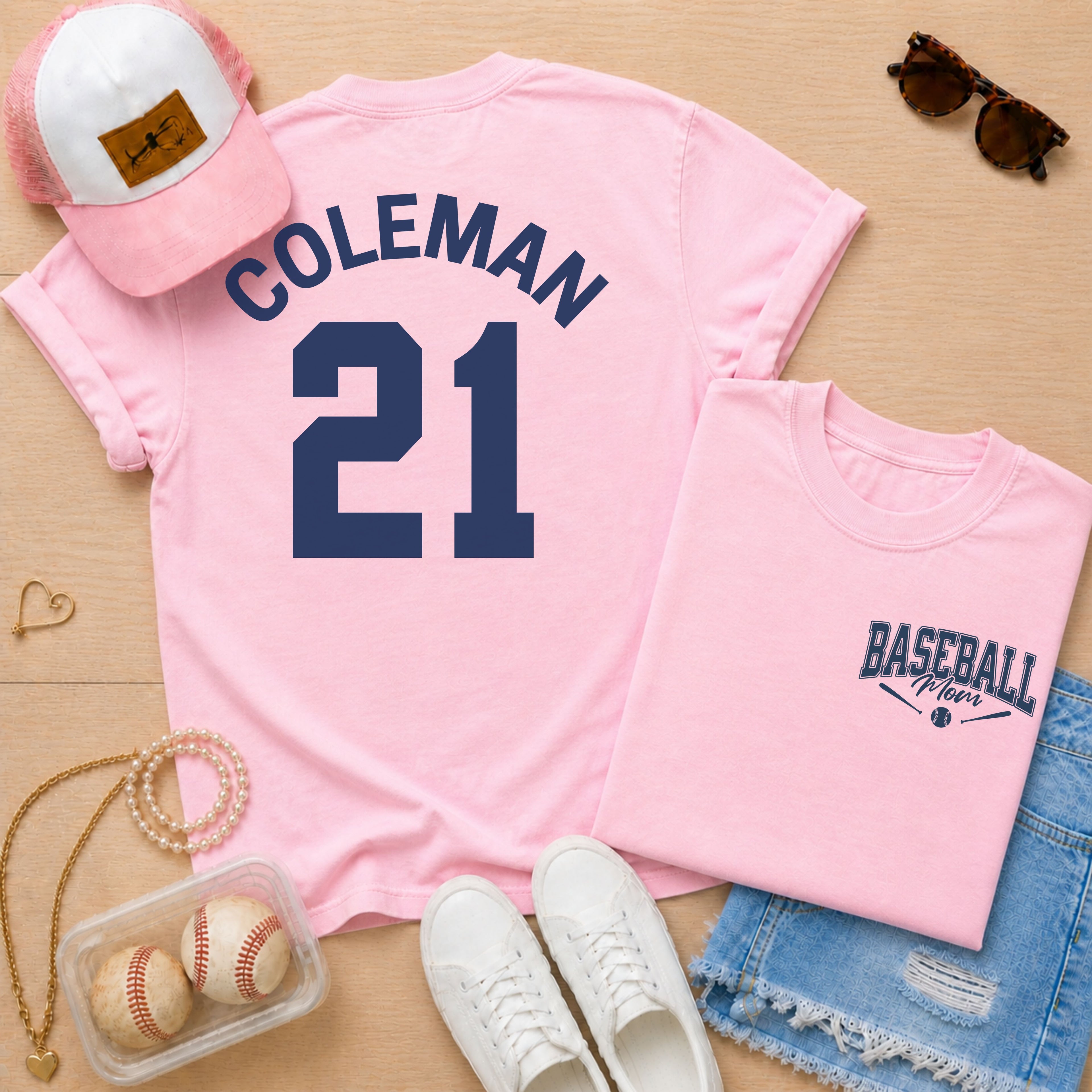 Pink t-shirt with 'COLEMAN 21' design, pink cap, sunglasses, and baseball-themed accessories on a wooden surface.