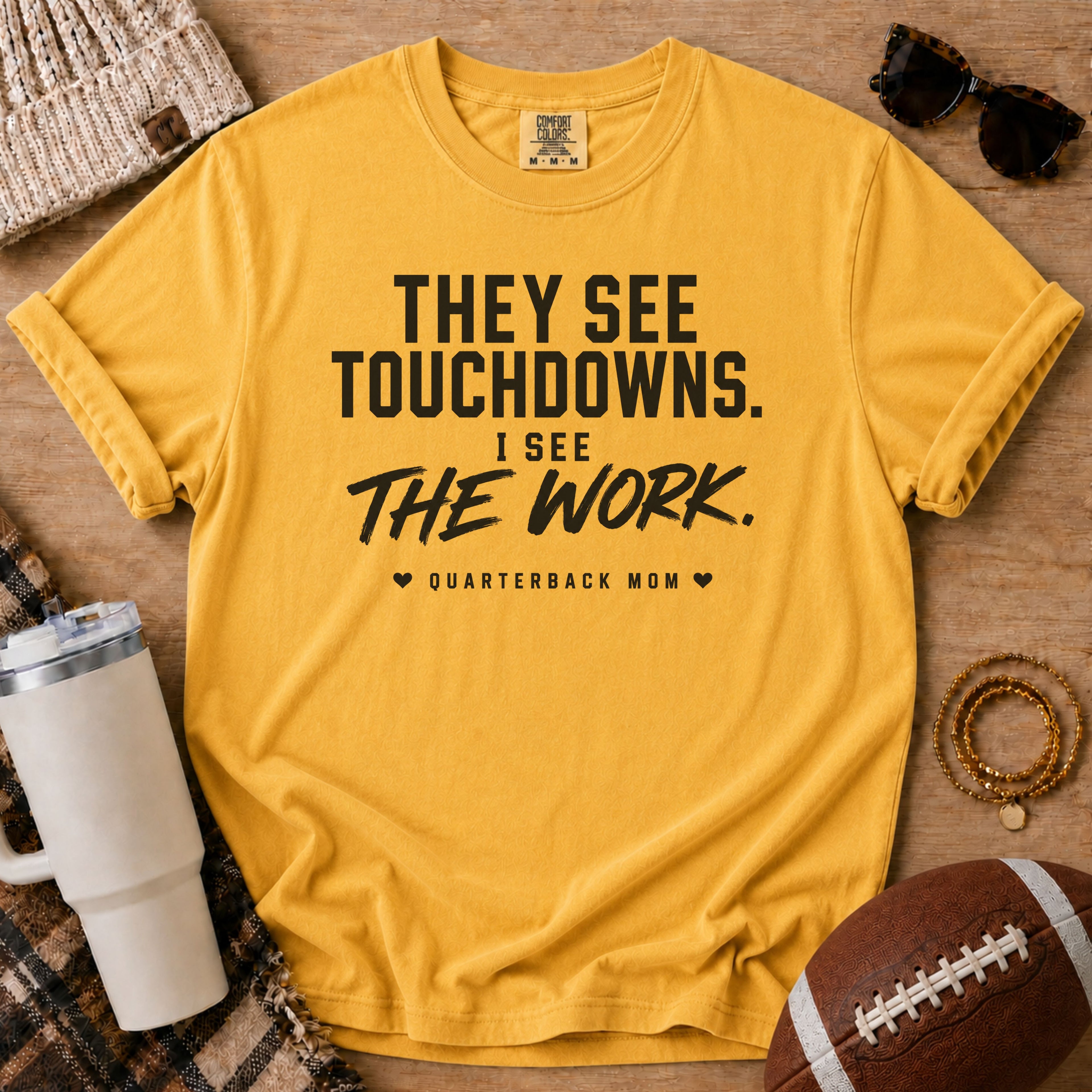 A yellow graphic t-shirt with black text reading 'THEY SEE TOUCHDOWNS. I SEE THE WORK.