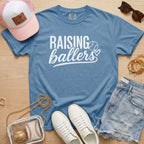 Raising Ballers baseball mom Comfort Colors blue jean game day tee styled with hat, denim shorts, and baseball accessories