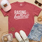 Raising Ballers baseball mom Comfort Colors crimson game day tee styled with hat, denim shorts, and baseball accessories