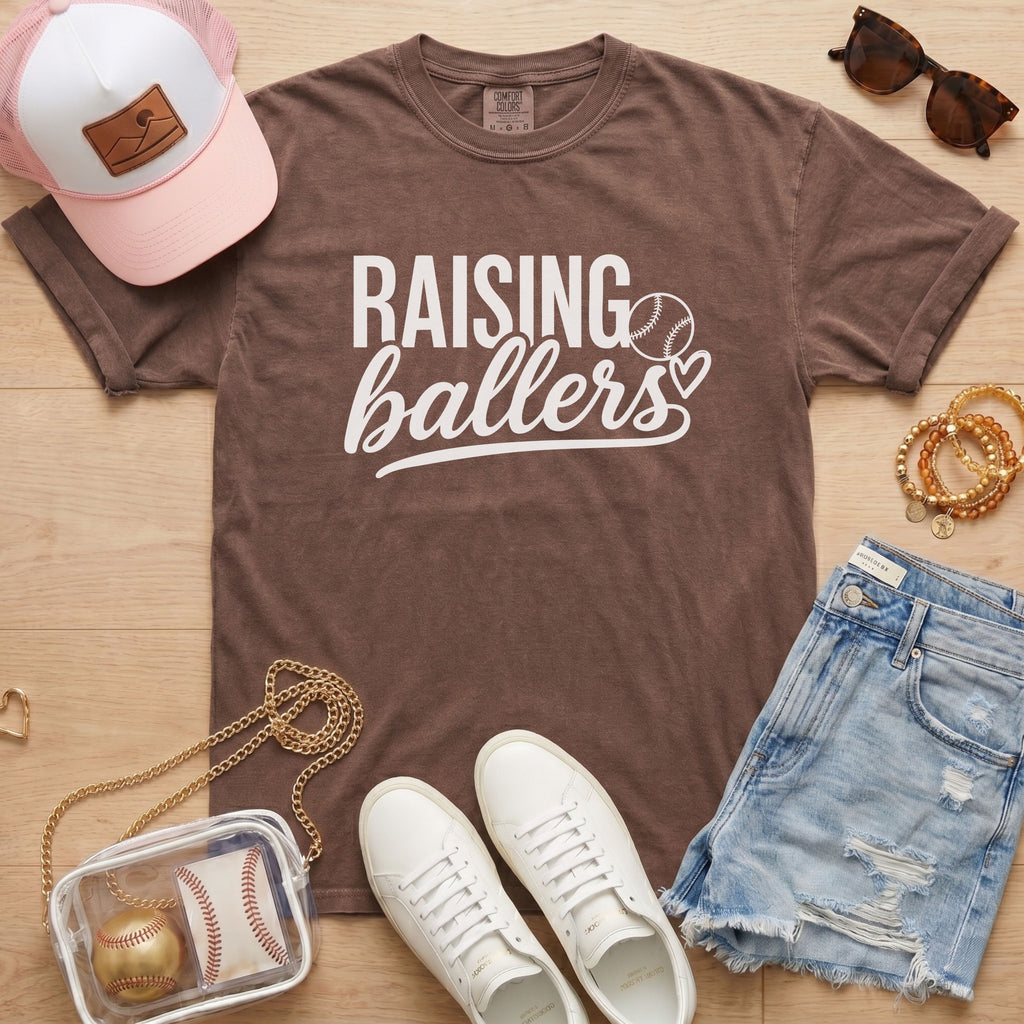 Raising Ballers baseball mom Comfort Colors espresso game day tee styled with hat, denim shorts, and baseball accessories