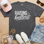 Raising Ballers baseball mom Comfort Colors pepper game day tee styled with hat, denim shorts, and baseball accessories