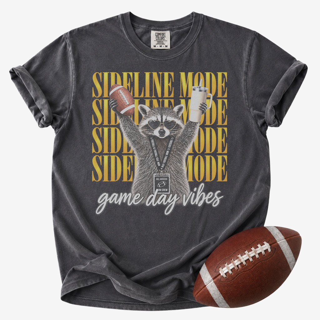 Football mom graphic T-shirt in charcoal gray, Comfort Colors Pepper, featuring a raccoon in heart sunglasses holding a football and tumbler with “Sideline Mode” and “Game Day Vibes” lettering.