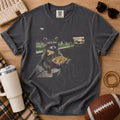 Charcoal gray football game day graphic tee, Comfort Colors Pepper, styled in a flat lay with a raccoon eating nachos near a football field and a football beside the shirt.