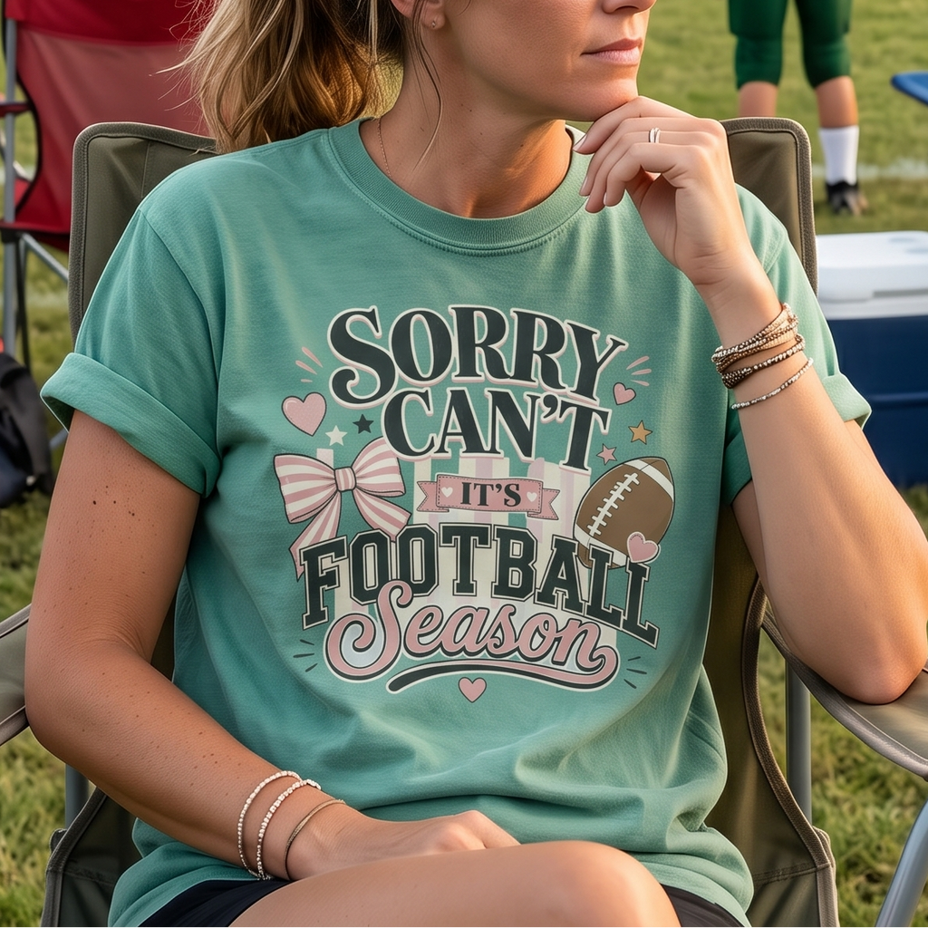 Football mom wearing a Light Green Sorry Can't It's Football Season shirt on the sideline at a youth football game.
