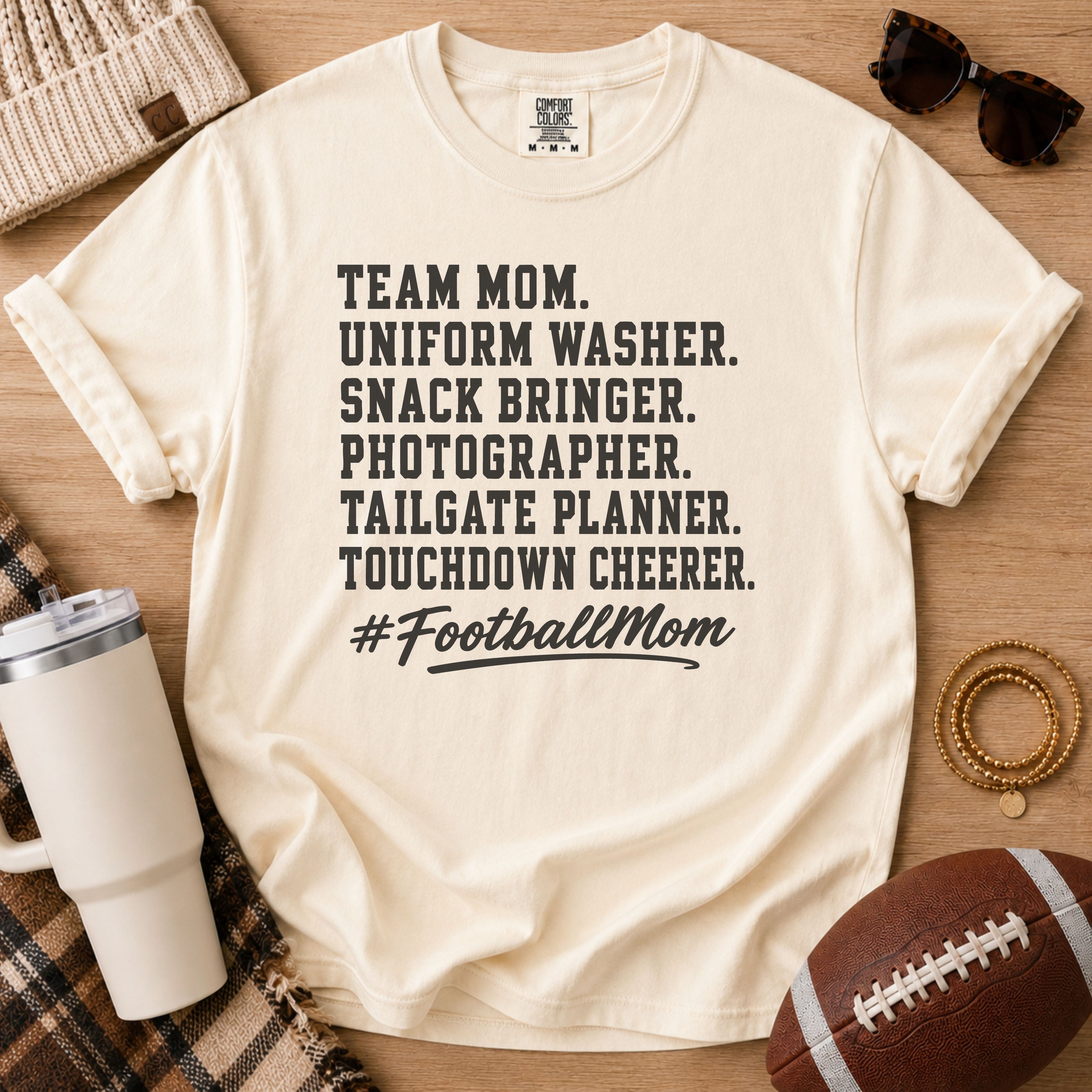 Super Football Mom football mom Comfort Colors tee in Ivory, flat lay with a football, tumbler, and sunglasses