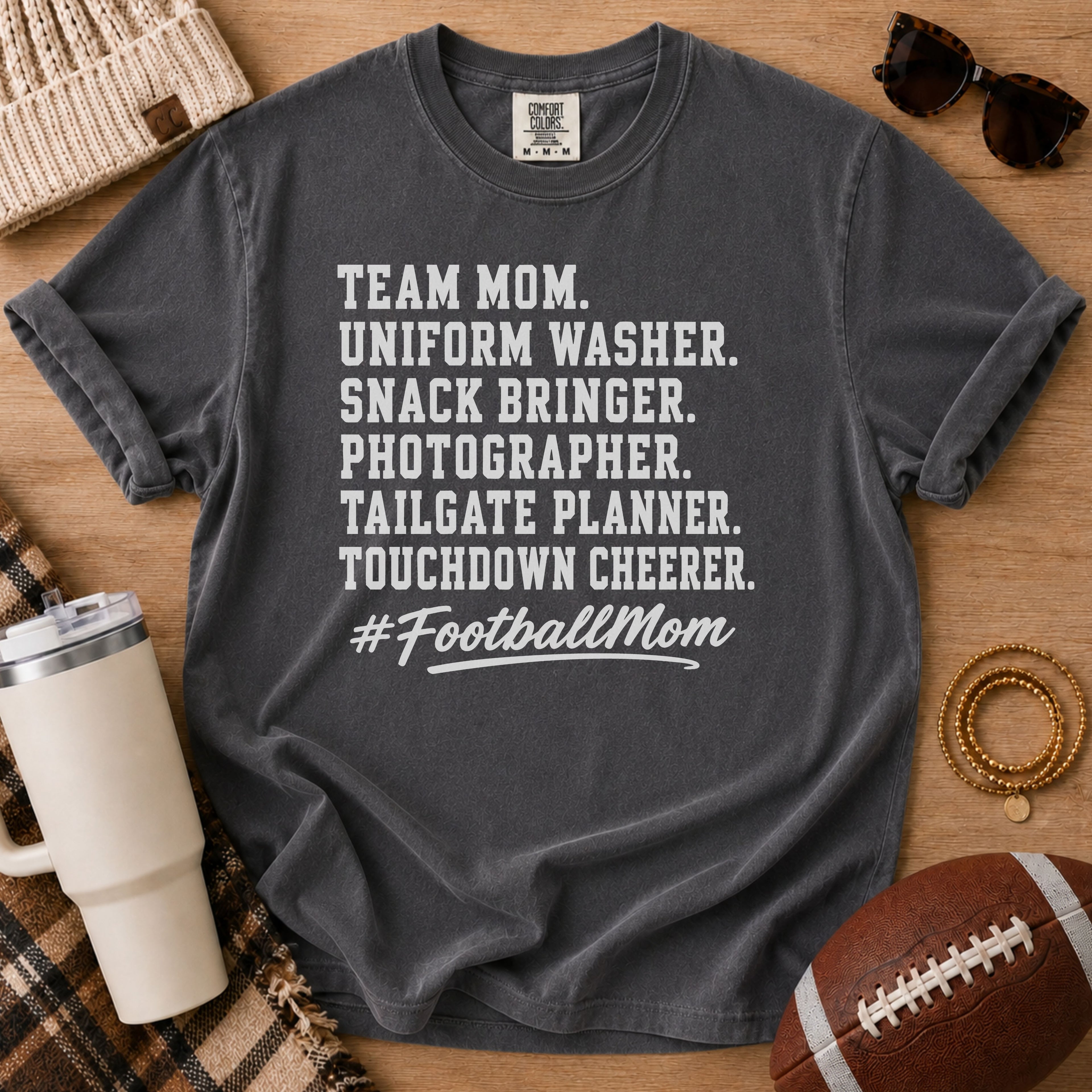 Super Football Mom football mom Comfort Colors tee in Pepper charcoal, flat lay with a football and accessories