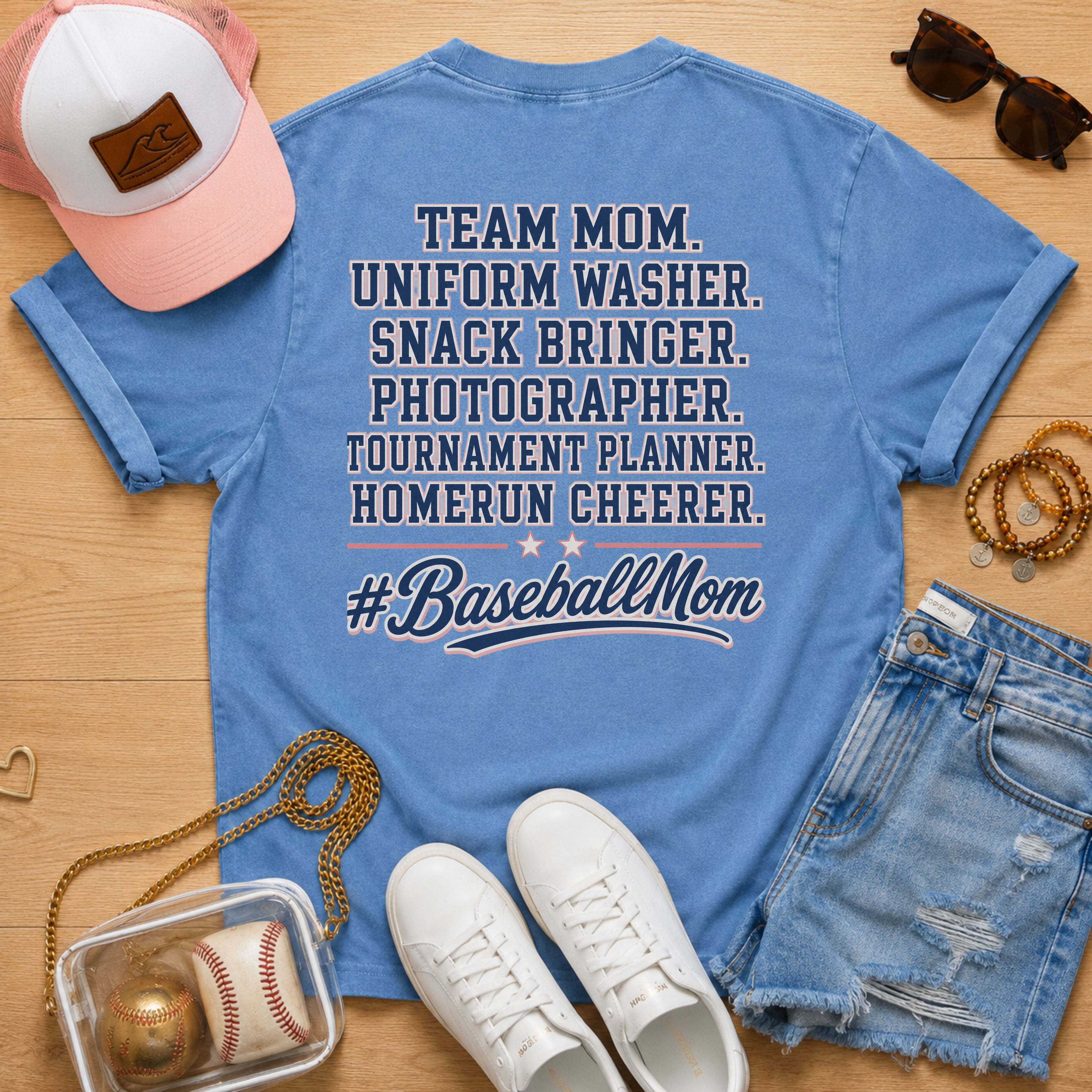 Team Mom Uniform Washer Snack Bringer baseball mom Comfort Colors Blue Jean tee flat lay with pink trucker hat, baseball purse, white sneakers, denim shorts, sunglasses, and jewelry.