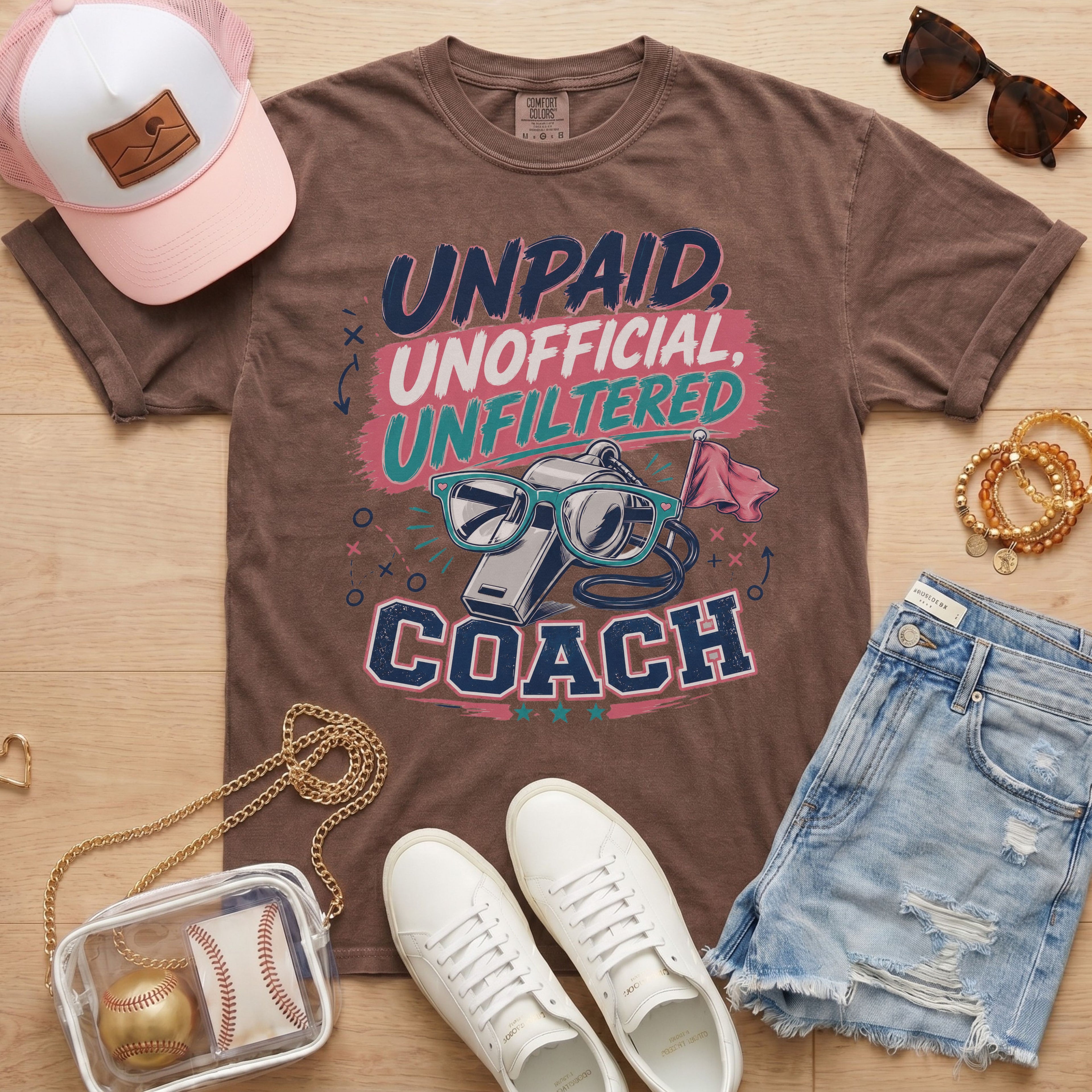 Unpaid Unofficial Unfiltered Coach Comfort Colors tee in espresso flat lay with trucker hat, denim shorts, and white sneakers.