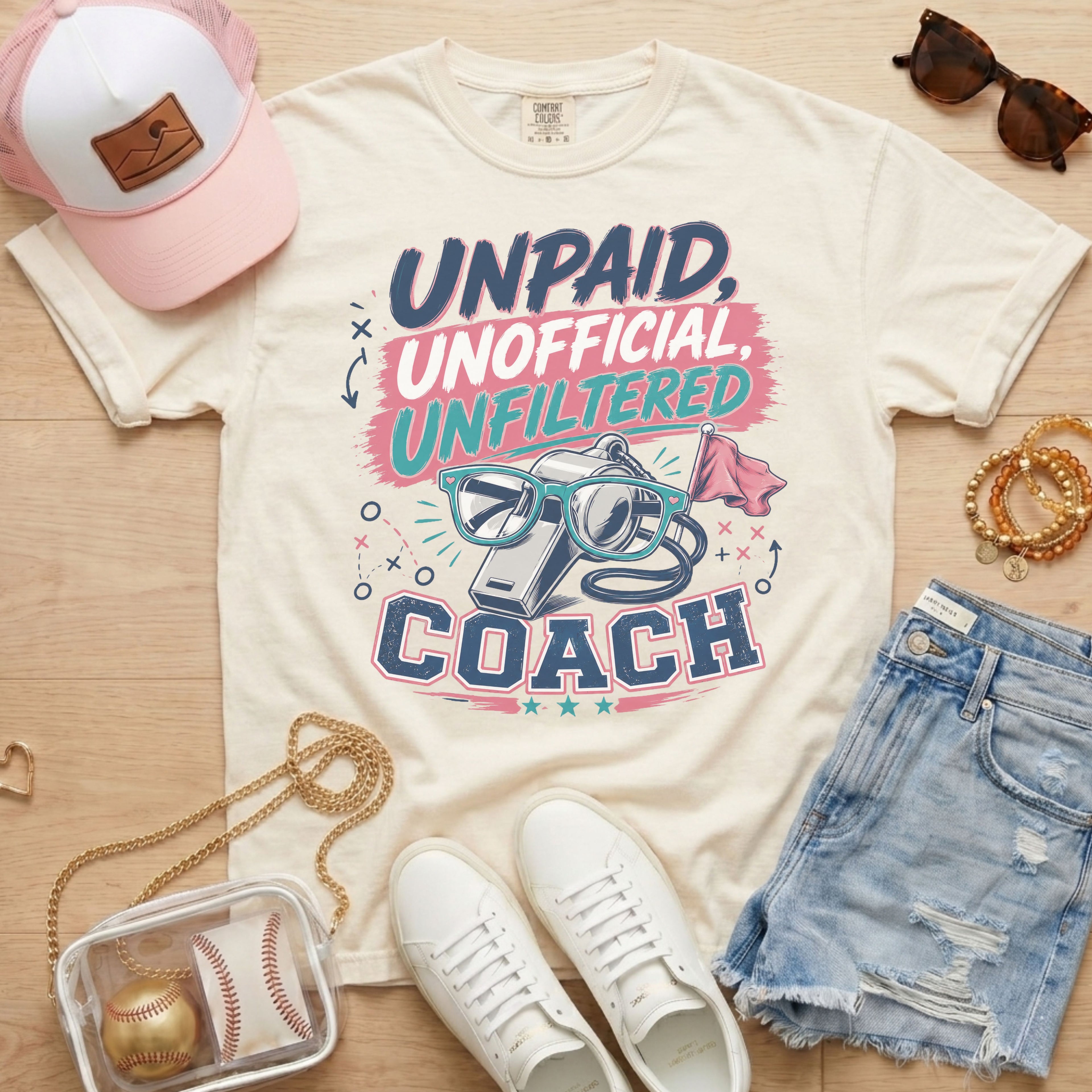 Unpaid Unofficial Unfiltered Coach Comfort Colors tee in ivory flat lay with trucker hat, denim shorts, and white sneakers.
