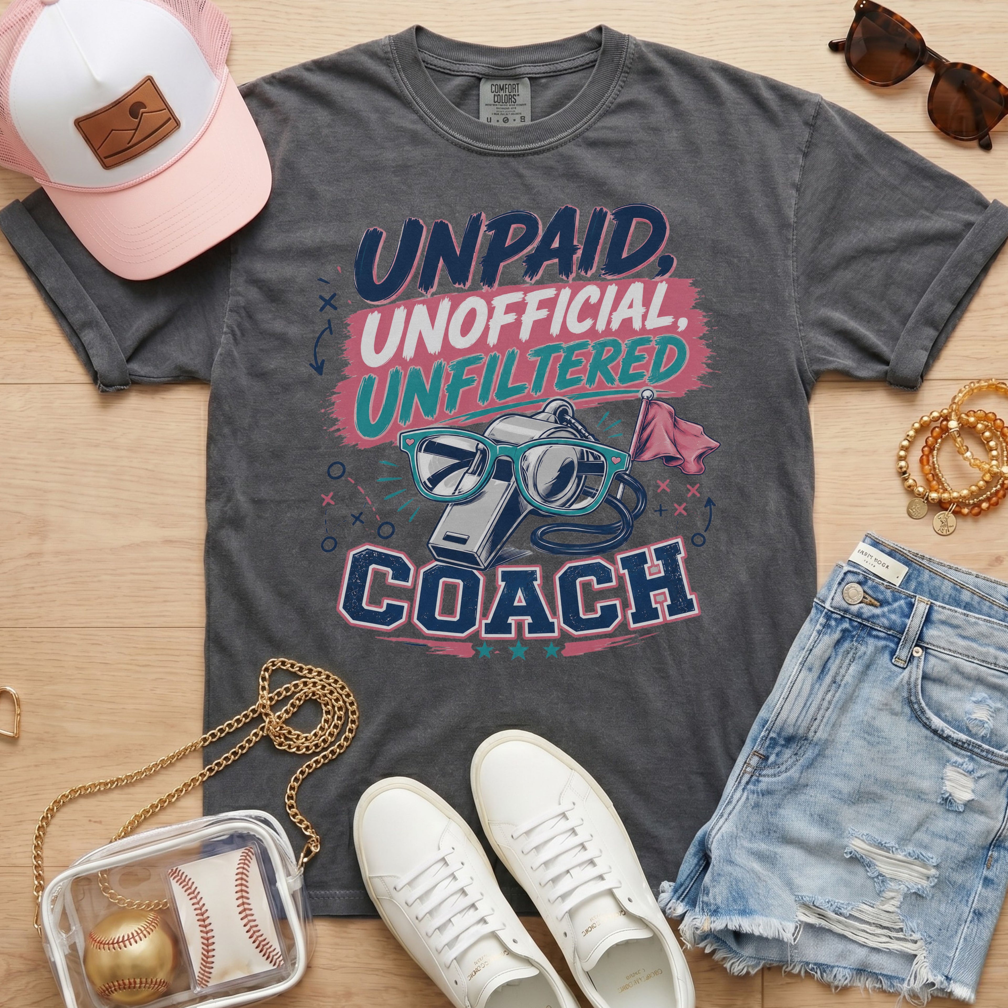 Unpaid Unofficial Unfiltered Coach Comfort Colors tee in pepper flat lay with trucker hat, denim shorts, and white sneakers.