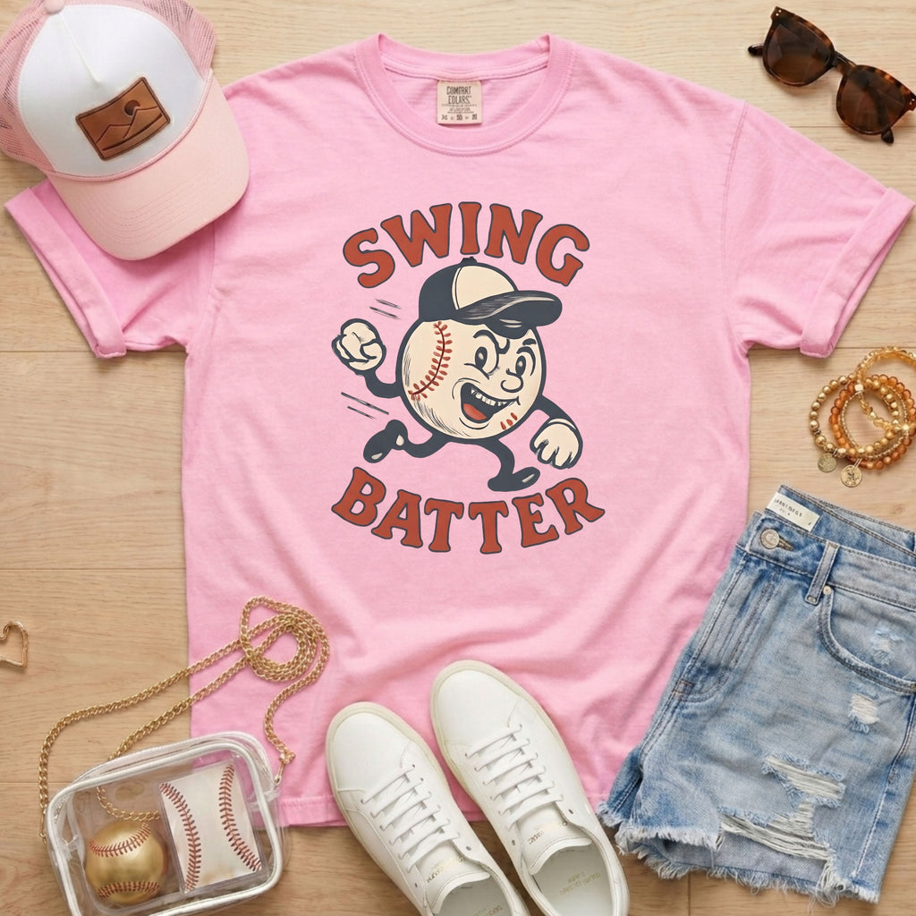 Pink t-shirt with 'Swing Batter' graphic, white sneakers, denim shorts, pink cap, and small bag on a wooden surface.