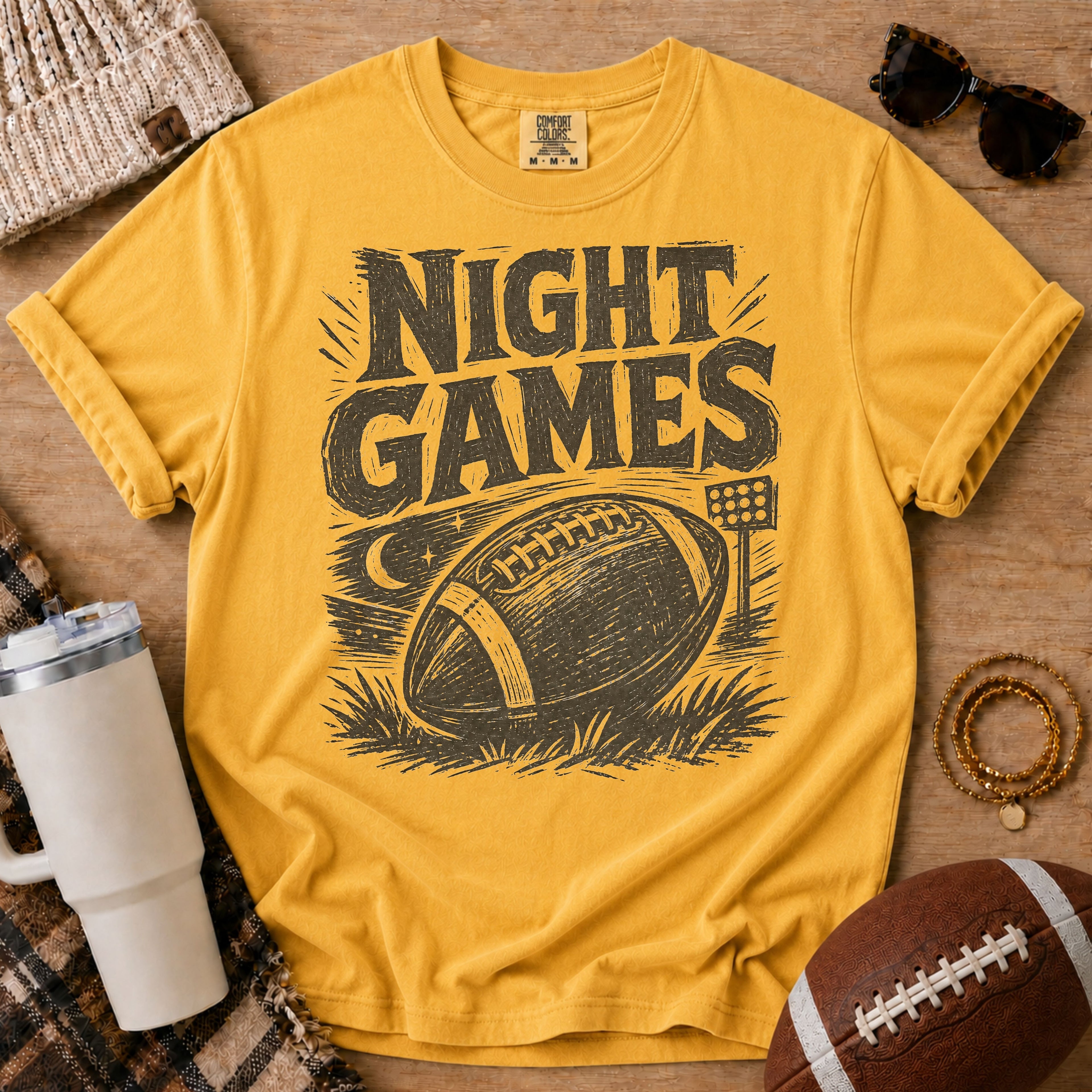 Golden yellow football graphic tee, Comfort Colors Mustard, styled with game day accessories and a distressed “Night Games” football design.