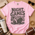Vintage football graphic T-shirt in light pink, Comfort Colors Blossom, styled in a game day flat lay with distressed “Night Games” lettering and a football illustration.
