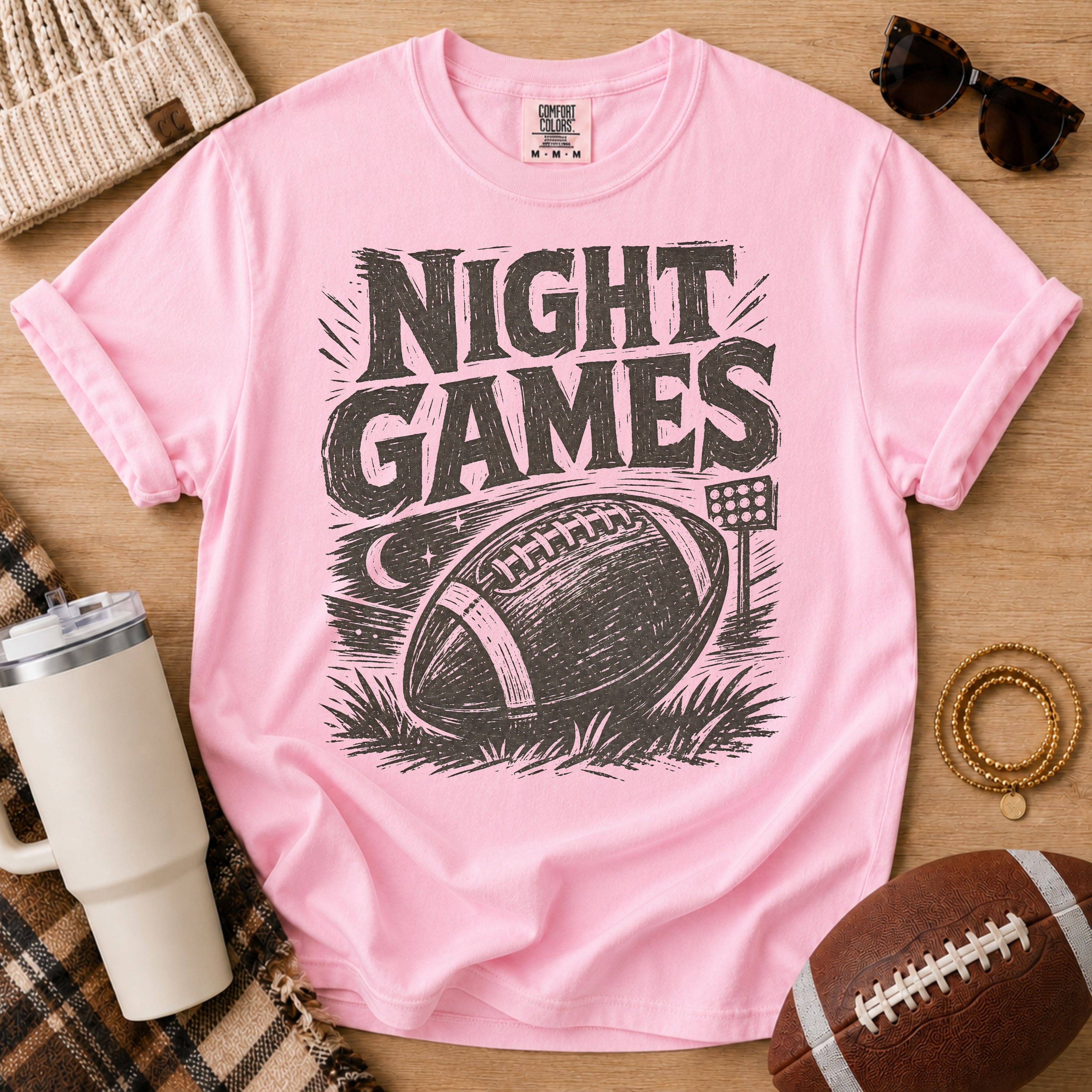Vintage football graphic T-shirt in light pink, Comfort Colors Blossom, styled in a game day flat lay with distressed “Night Games” lettering and a football illustration.