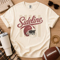 Cream football game day graphic tee, Comfort Colors Ivory, styled in a flat lay with a football and distressed “Sideline” helmet design.